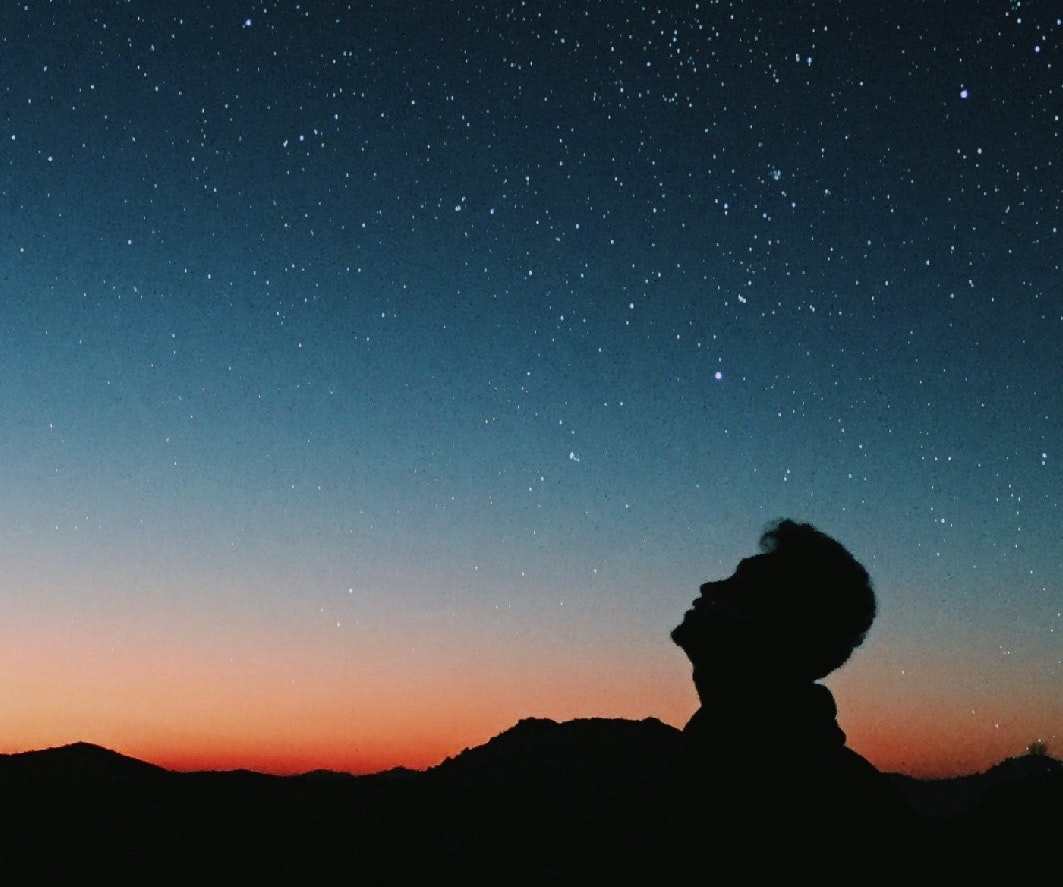Image of human staring up at stars at dusk, representing 