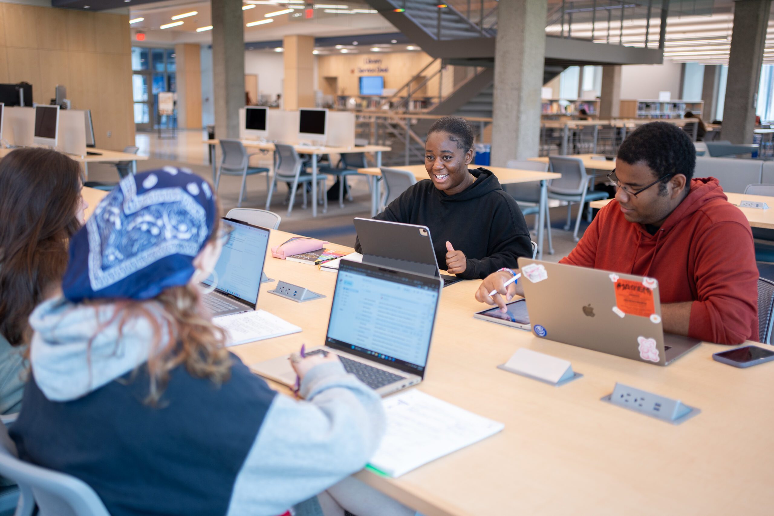 Four students study together at a table in Milne Library. One is smiling.
