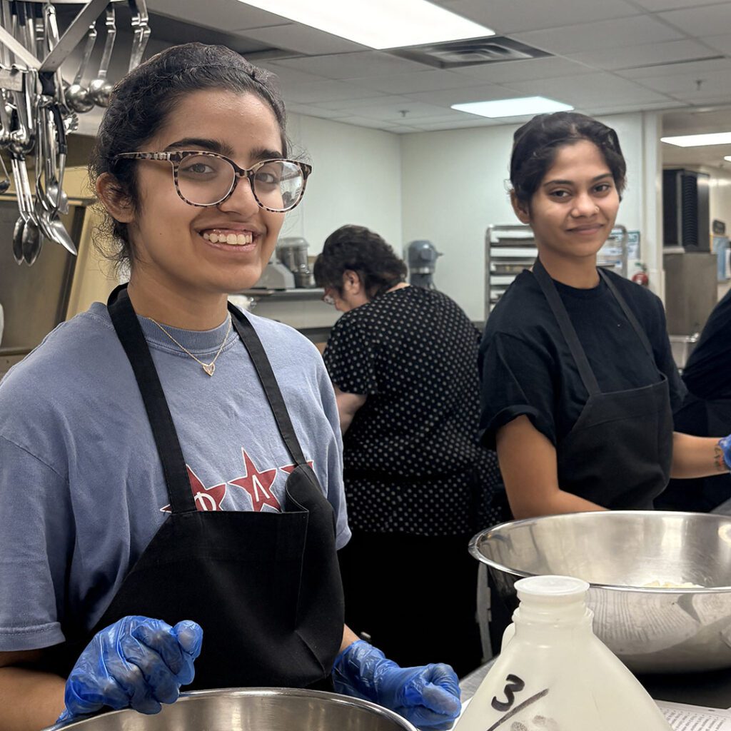 Two students smile as they prepare food for their cultural group's dinner event.